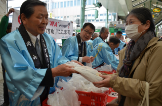 青江会長（左）からきぬむすめ・にこまるを受け取る商店街利用者（25日、岡山市で）